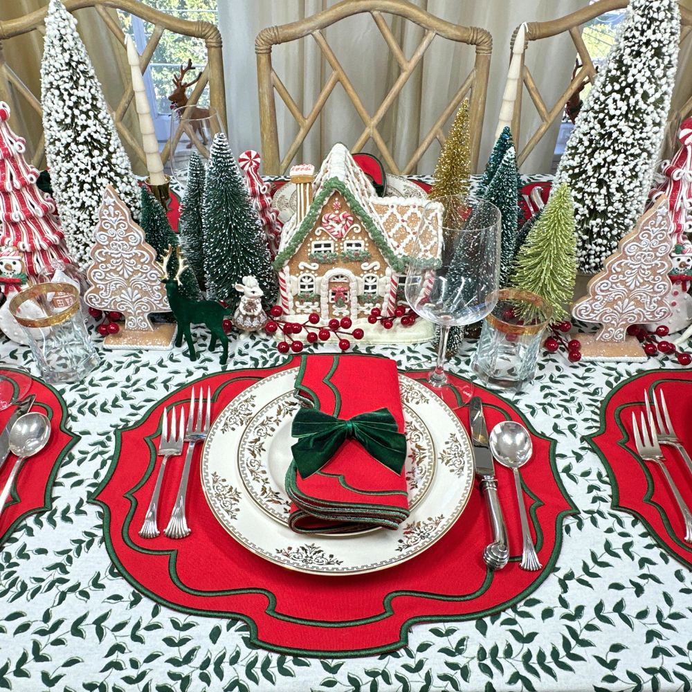 Christmas-themed table setting with gingerbread house, trees, and red placemats.